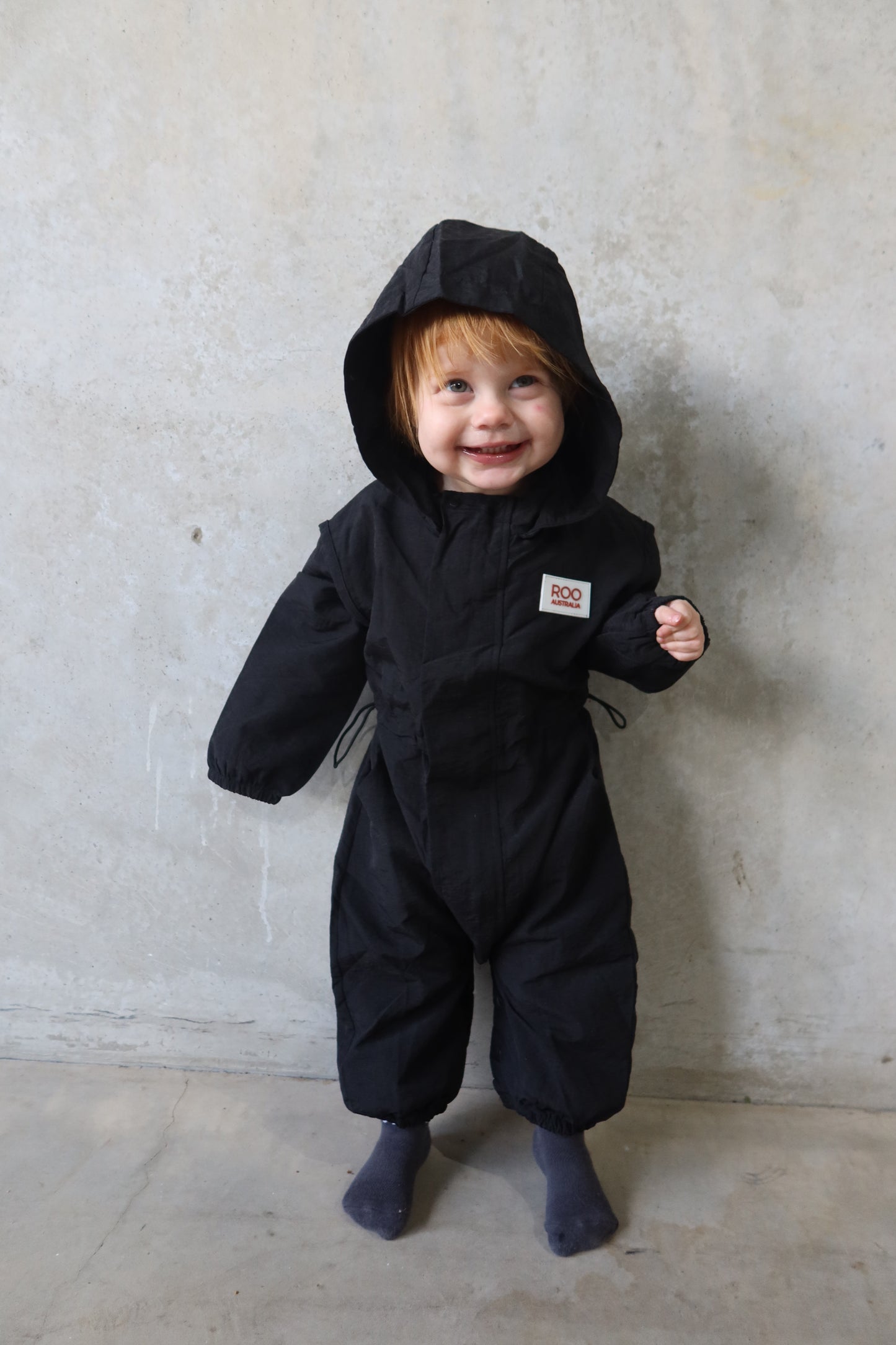 front view of toddler in full black boiler suit, showcasing centre zip and relaxed fit.
